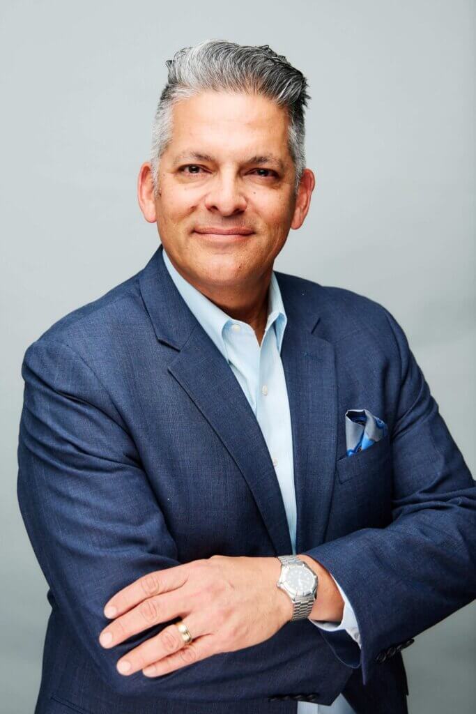 Portrait of a middle-aged man in a blue suit with a light blue shirt, arms crossed, looking at the camera.
