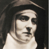 Portrait of a Catholic nun in a black habit and white wimple, looking downward with a solemn expression.