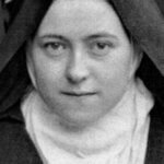 Portrait of a nun in a dark habit and white wimple, looking straight ahead.