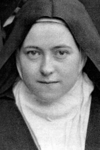 Portrait of a nun in a dark habit and white wimple, looking straight ahead.